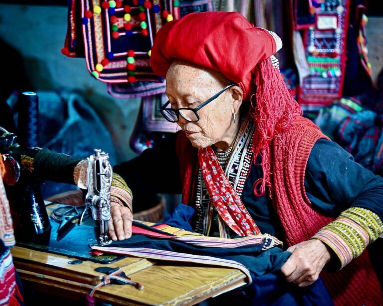 A woman from the “Red Dao” branch of the Dao ethnic minority, sewing clothing at the Sa Pa market in…